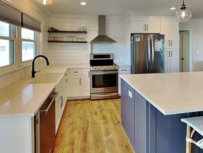 A modern kitchen with white cabinetry, stainless steel appliances, and a wooden floor.