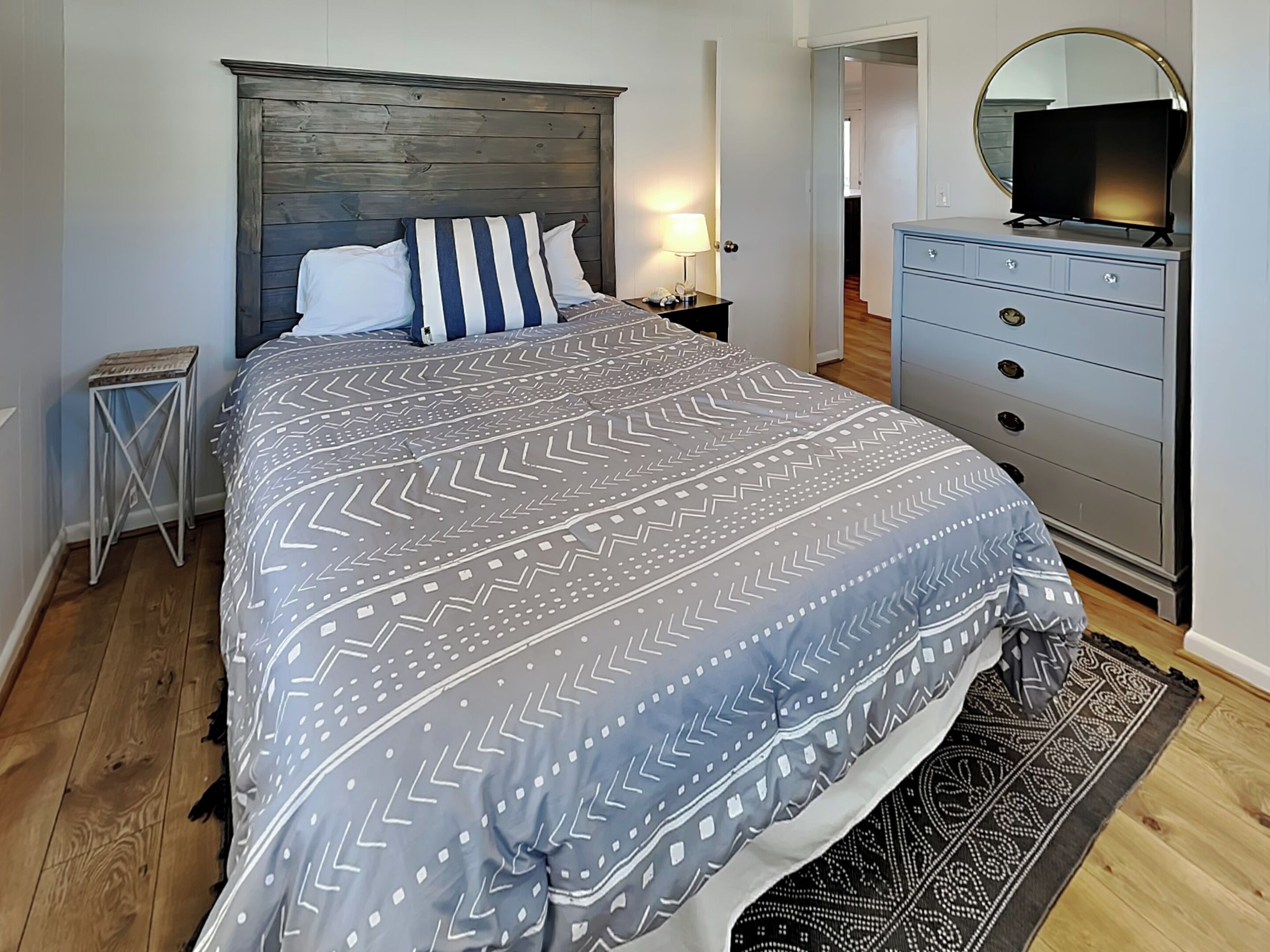 Un dormitorio con cama, cómoda, mesita de noche, lámpara y espejo.