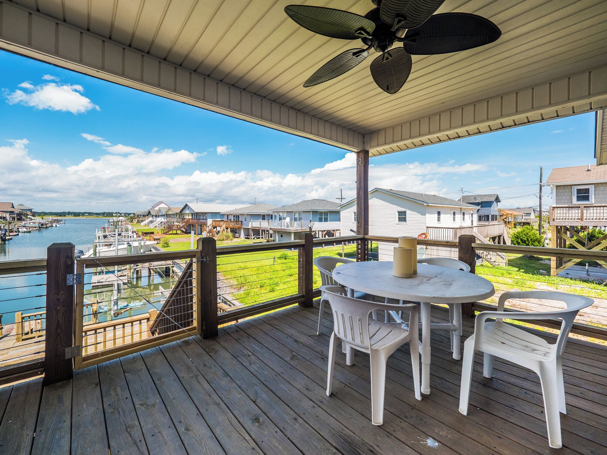 Um terraço coberto ao ar livre com mesa e cadeiras, com vista para uma marina e casas.