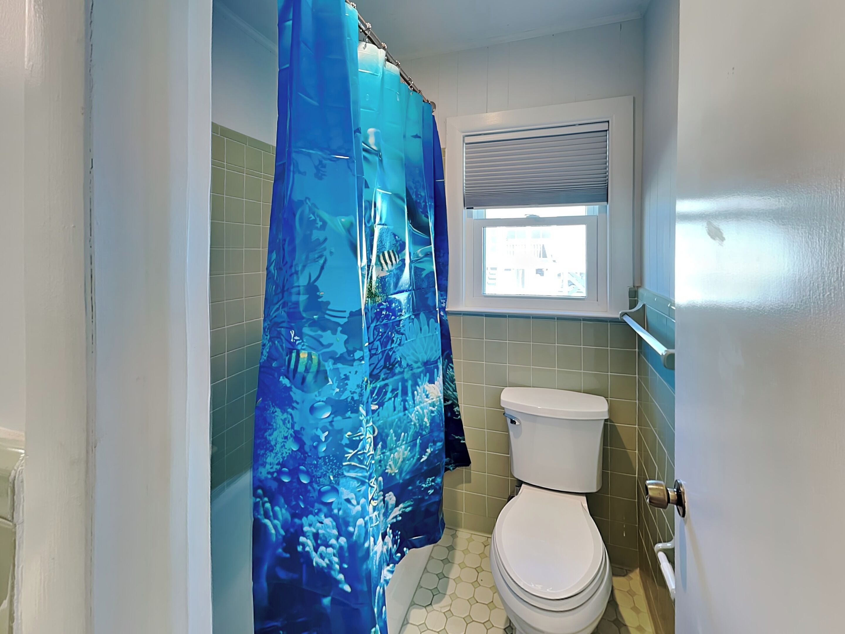Ein Badezimmer mit Toilette, Fenster und blauer Duschvorhang.