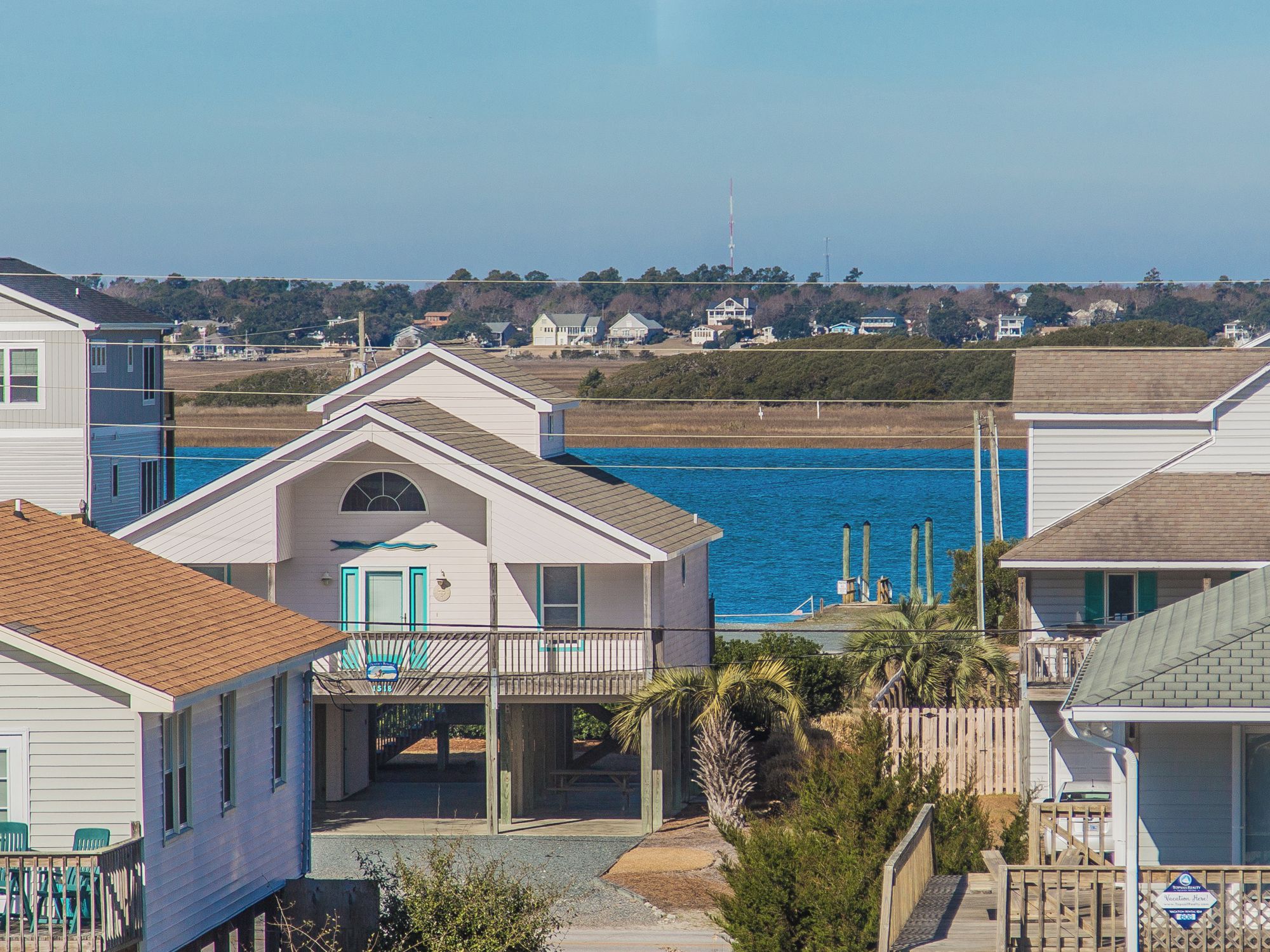 A coastal house with a balcony overlooking the sea, a wooden deck, and a clear view of the ocean.