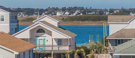 A coastal house with a balcony overlooking the sea, a wooden deck, and a clear view of the ocean.
