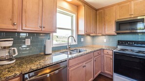 A kitchen with wooden cabinets, a stainless steel dishwasher, a granite countertop, a built-in oven, and a microwave. - Sunset Bay by Topsail Realty (Sneads Ferry)