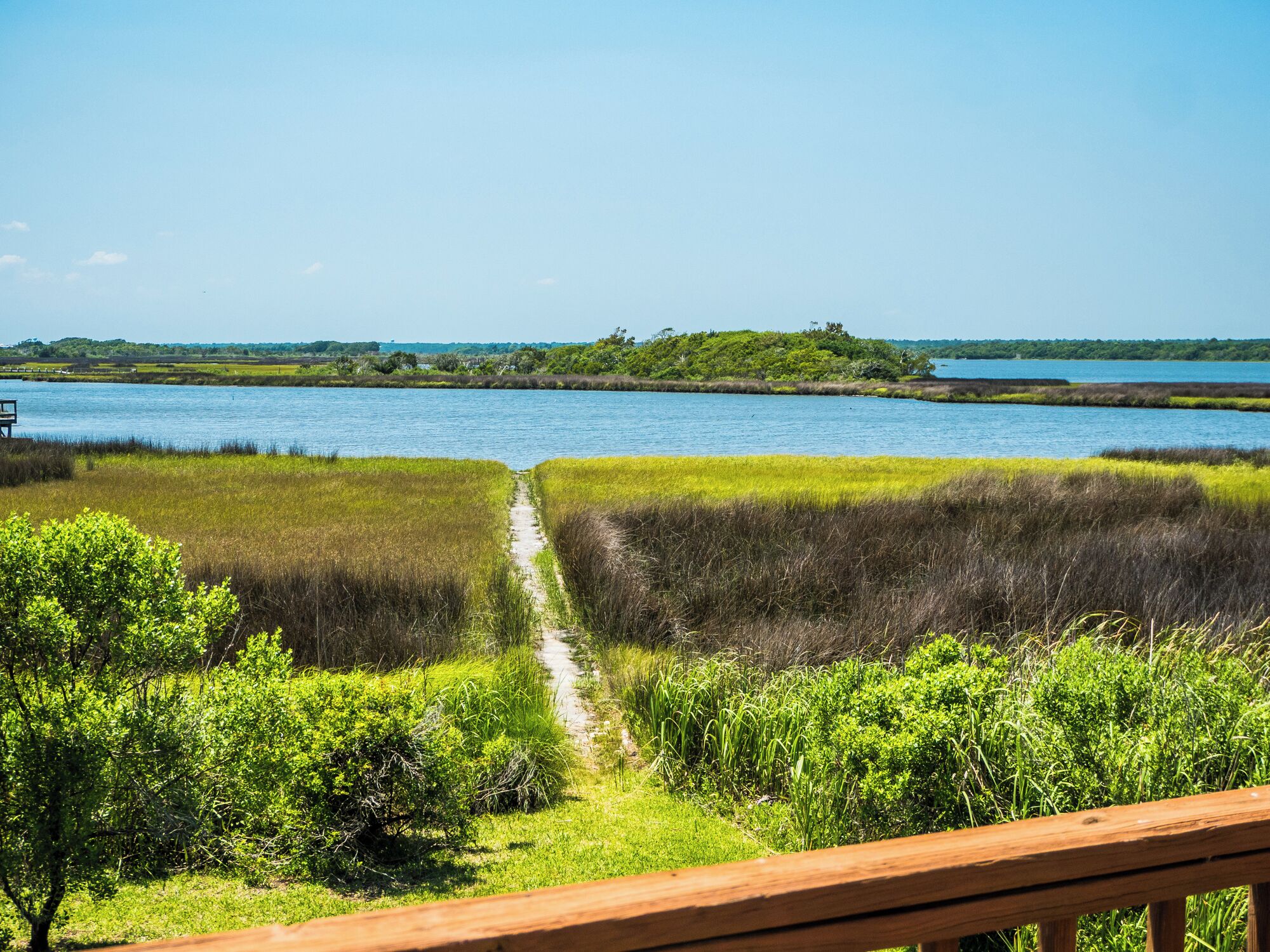 A pathway leading to a body of water with grassy banks and a wooden deck in the foreground.