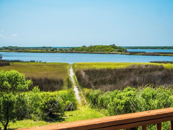 A pathway leading to a body of water with grassy banks and a wooden deck in the foreground. - Sunset Bay by Topsail Realty (Sneads Ferry)
