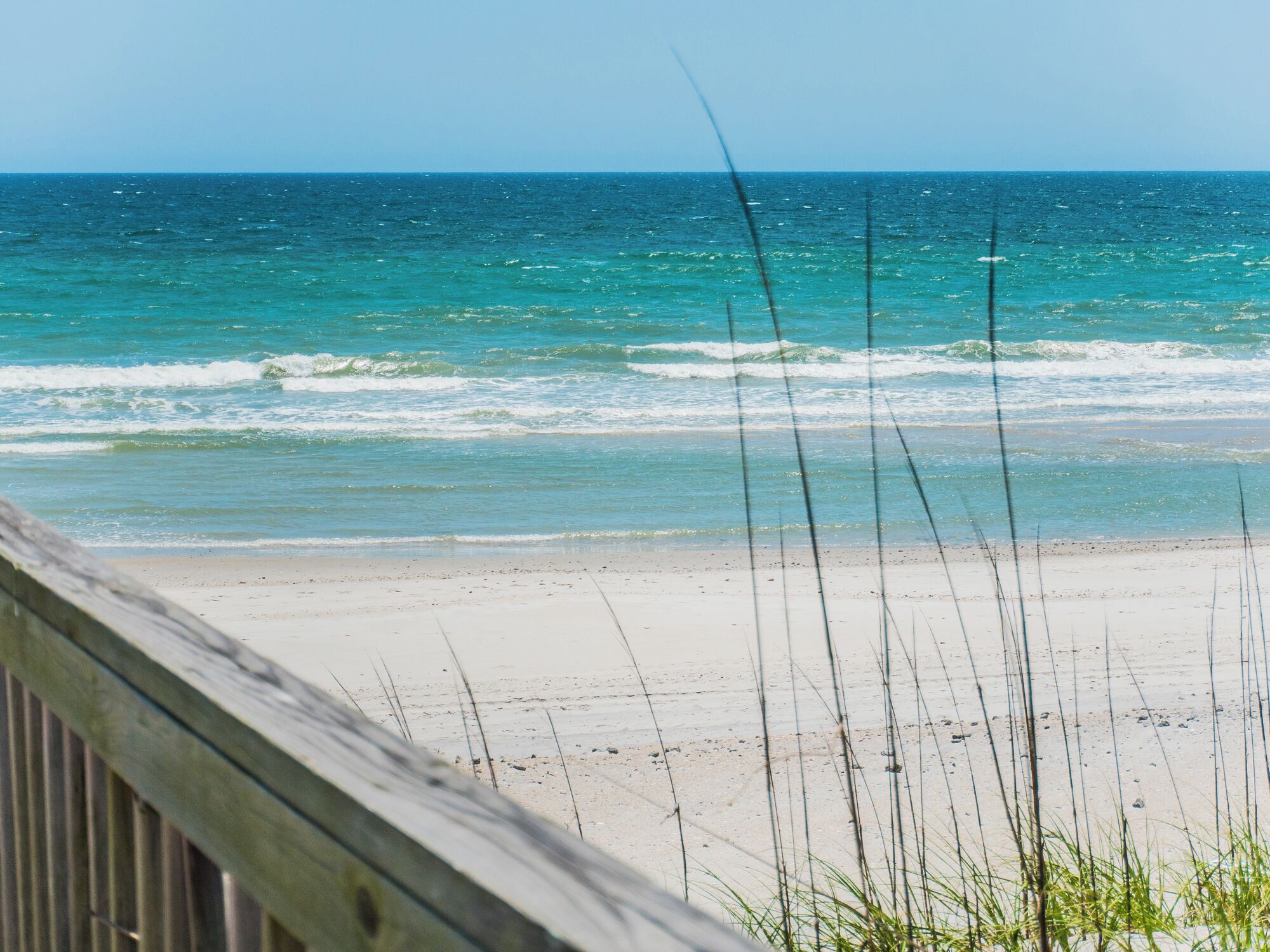 A beach with clear blue water and a wooden boardwalk leading to the shore.
