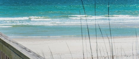 A beach with clear blue water and a wooden boardwalk leading to the shore.