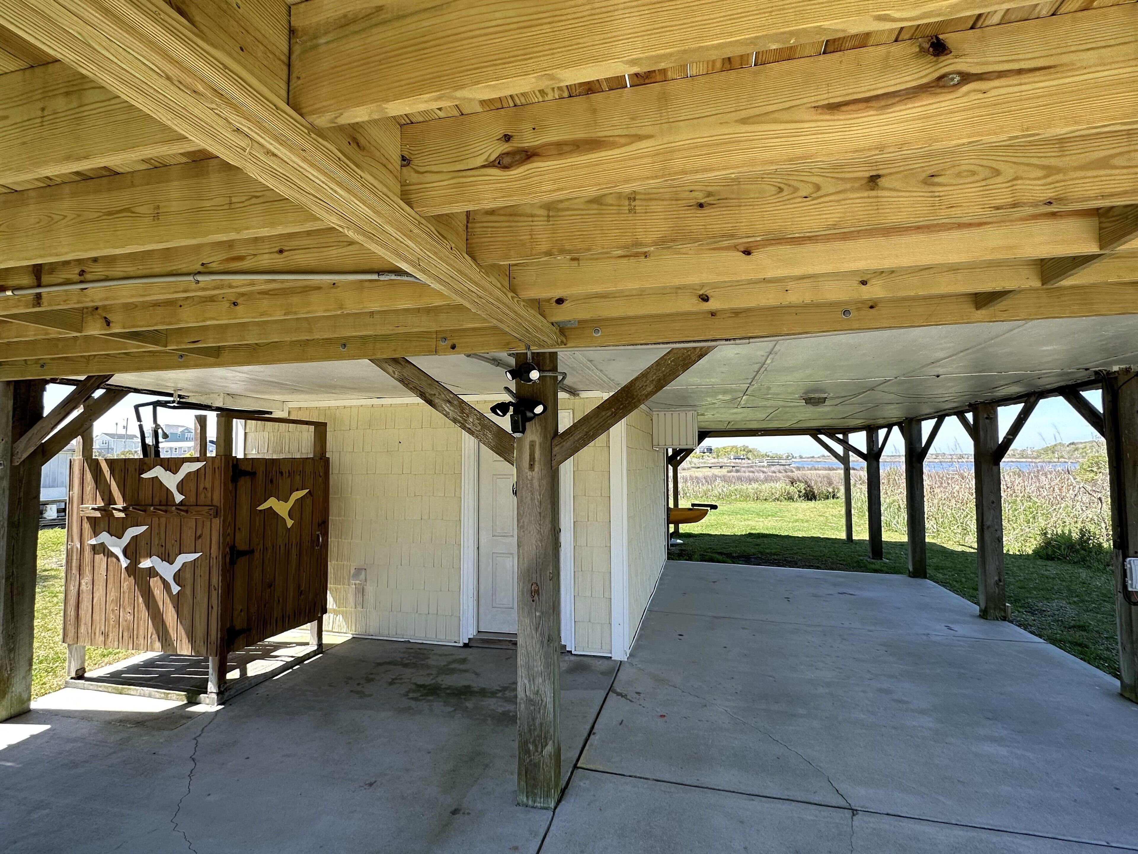 Un espace extérieur abrité, doté de poutres en bois, d’un sol en béton et offrant une vue sur le paysage.