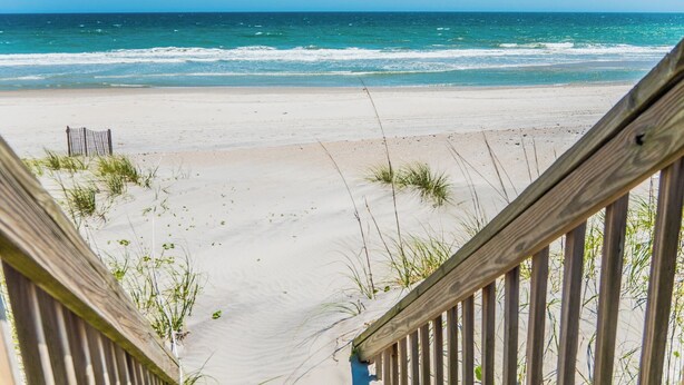 A wooden staircase leading to a sandy beach with the ocean in the background. - Sunset Bay by Topsail Realty (Sneads Ferry)