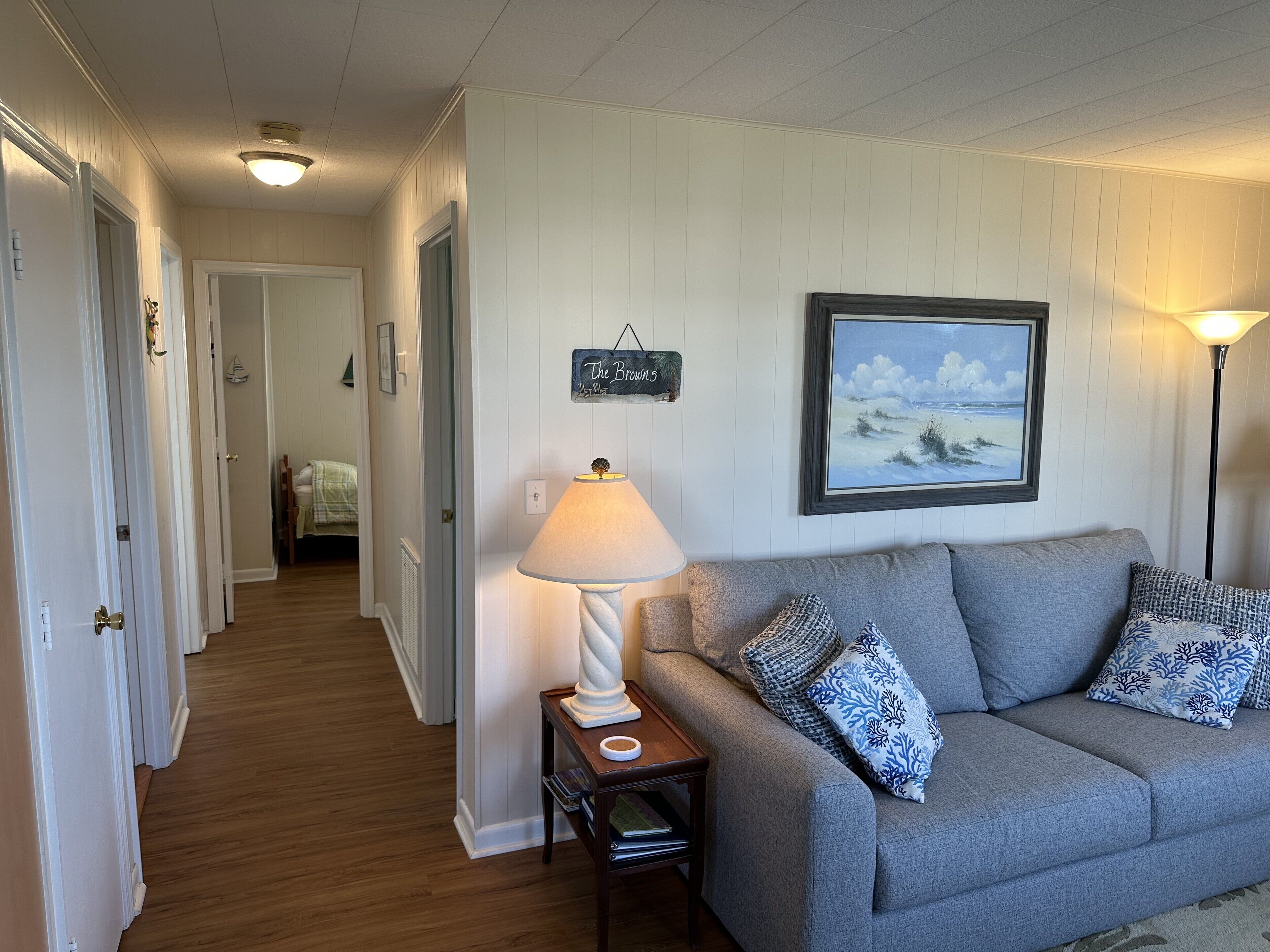 A hallway with a grey sofa, a lamp, and a painting on the wall.
