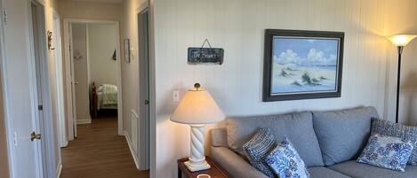 A hallway with a grey sofa, a lamp, and a painting on the wall.