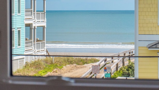 A coastal view with a beach, a wooden pier, and a building with a balcony.