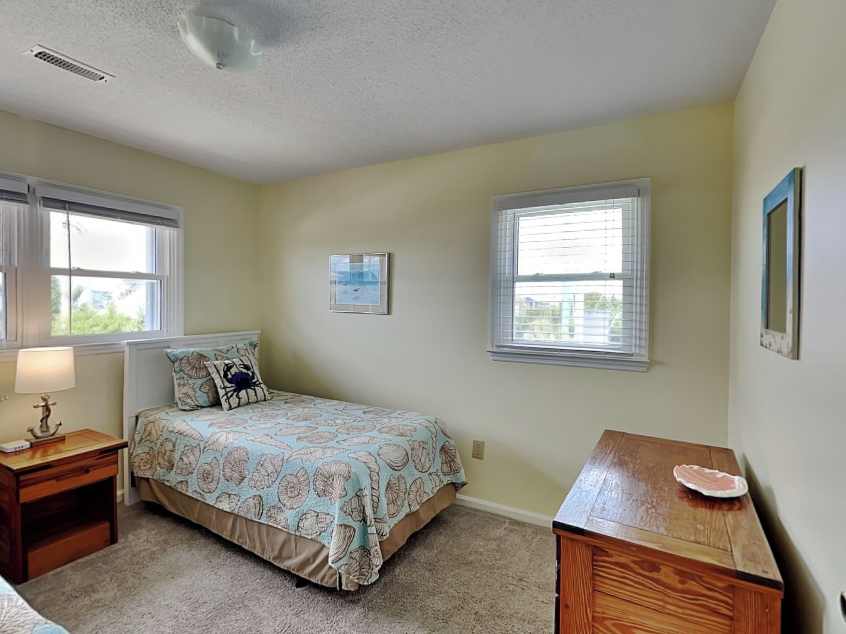 A bedroom with a bed, a nightstand, a dresser, and two windows.