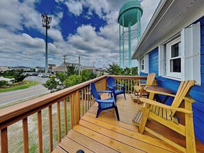 A wooden deck with chairs and a table, a water tower, and a building with blue siding.