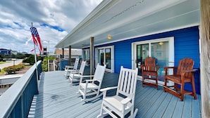 A deck with white and brown Adirondack chairs, a blue building, and an American flag.
