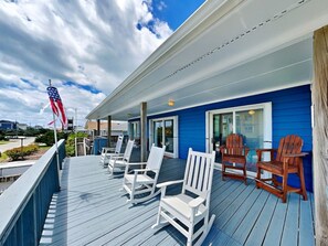 A deck with white and brown Adirondack chairs, a blue building, and an American flag.