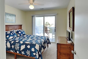 A bedroom with a bed, a ceiling fan, a sliding glass door to a balcony, and a wooden dresser.