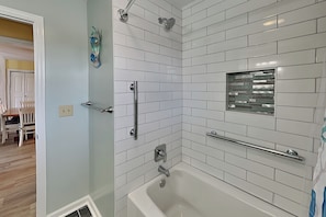 A bathroom with white tiled walls, a bathtub, a shower with a glass enclosure, and a towel rack.