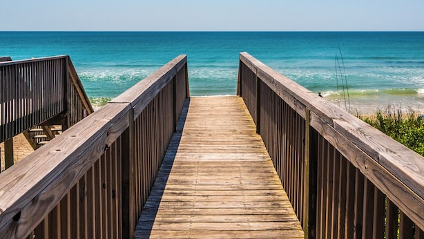 Une promenade en bois qui mène à l’océan et offre une vue dégagée sur la mer.