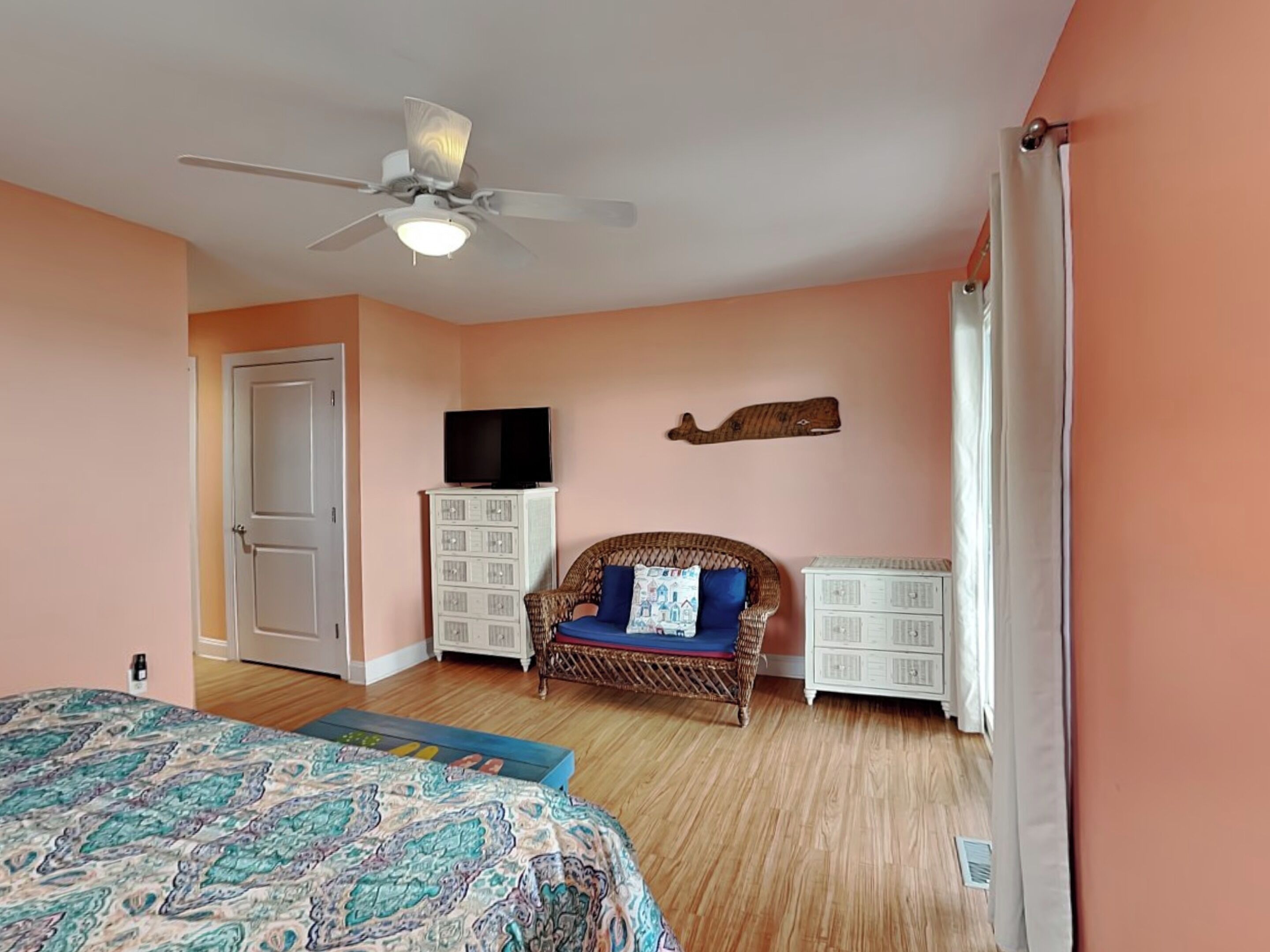 A bedroom with a bed, a ceiling fan, a television on a cabinet, and a wicker chair with a cushion.