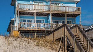 Un immeuble à plusieurs étages situé en bord de mer, doté de balcons et d’un escalier en bois menant à l’entrée.