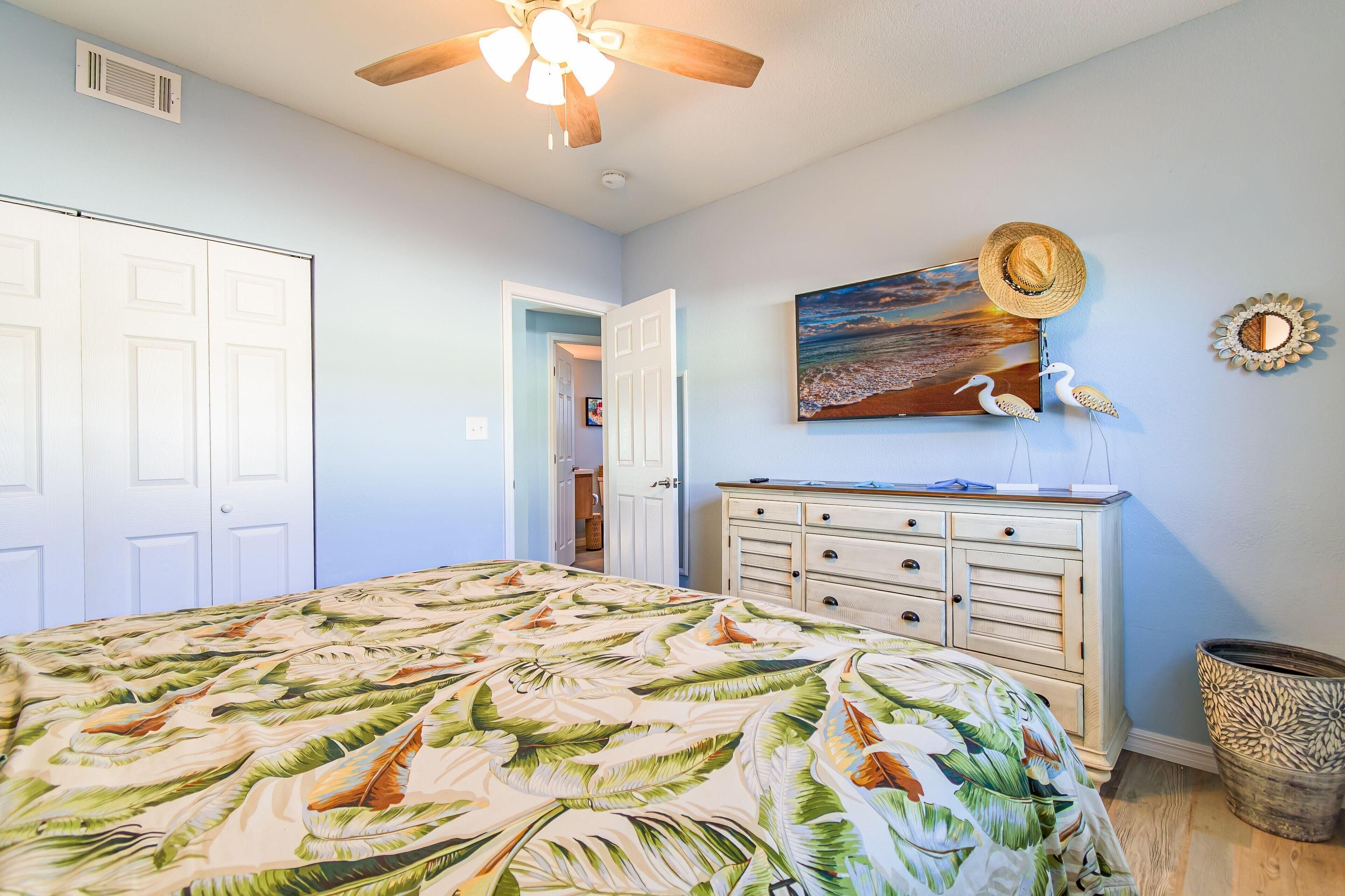 A bedroom with a bed, a dresser, a ceiling fan, and a painting on the wall.