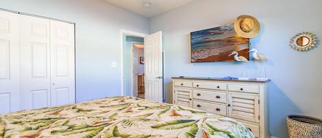 A bedroom with a bed, a dresser, a ceiling fan, and a painting on the wall.