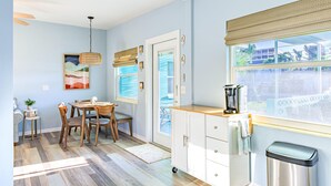 A modern kitchen with a dining area, featuring a wooden table and chairs, a coffee maker, and a view through the window. - Se La Vie (Treasure Island)