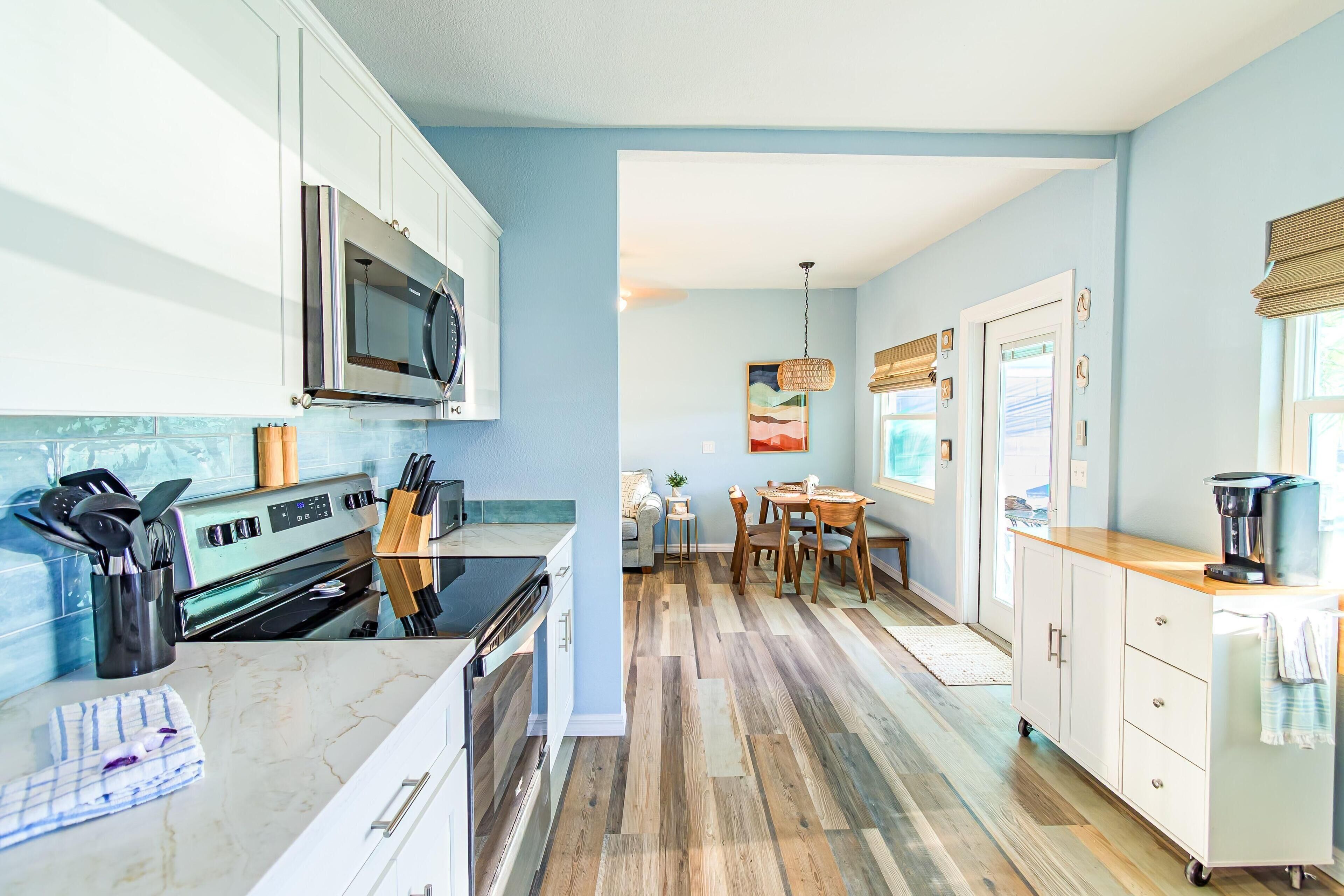 A kitchen with white cabinets, a microwave, and a stove. There is a dining area with a table and chairs.