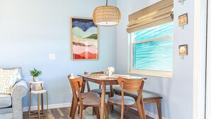 A dining area with a wooden table and chairs, a hanging light fixture, a framed artwork, and a window with a view. - Se La Vie (Treasure Island)