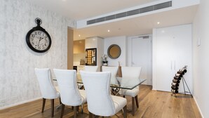 A dining area with a glass table and four chairs, a wall clock, a mirror, and a wine rack.