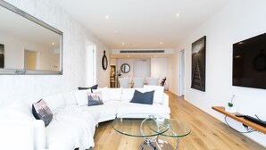 A modern living room with a white sectional sofa, a glass coffee table, and a large mirror on the wall.
