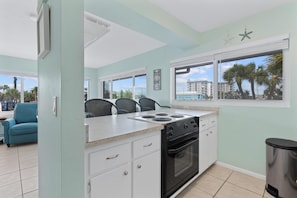 A kitchen with a stove, oven, and large windows. - Crescent Shore 201 (Fort Myers Beach)