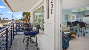 A balcony with a view of a busy street, a seating area with chairs and a table, and a kitchen area with chairs and a counter. - Crescent Shore 201 (Fort Myers Beach)