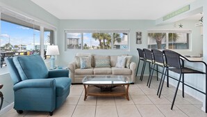 A living room with a sofa, a glass coffee table, and a dining area with chairs. - Crescent Shore 201 (Fort Myers Beach)