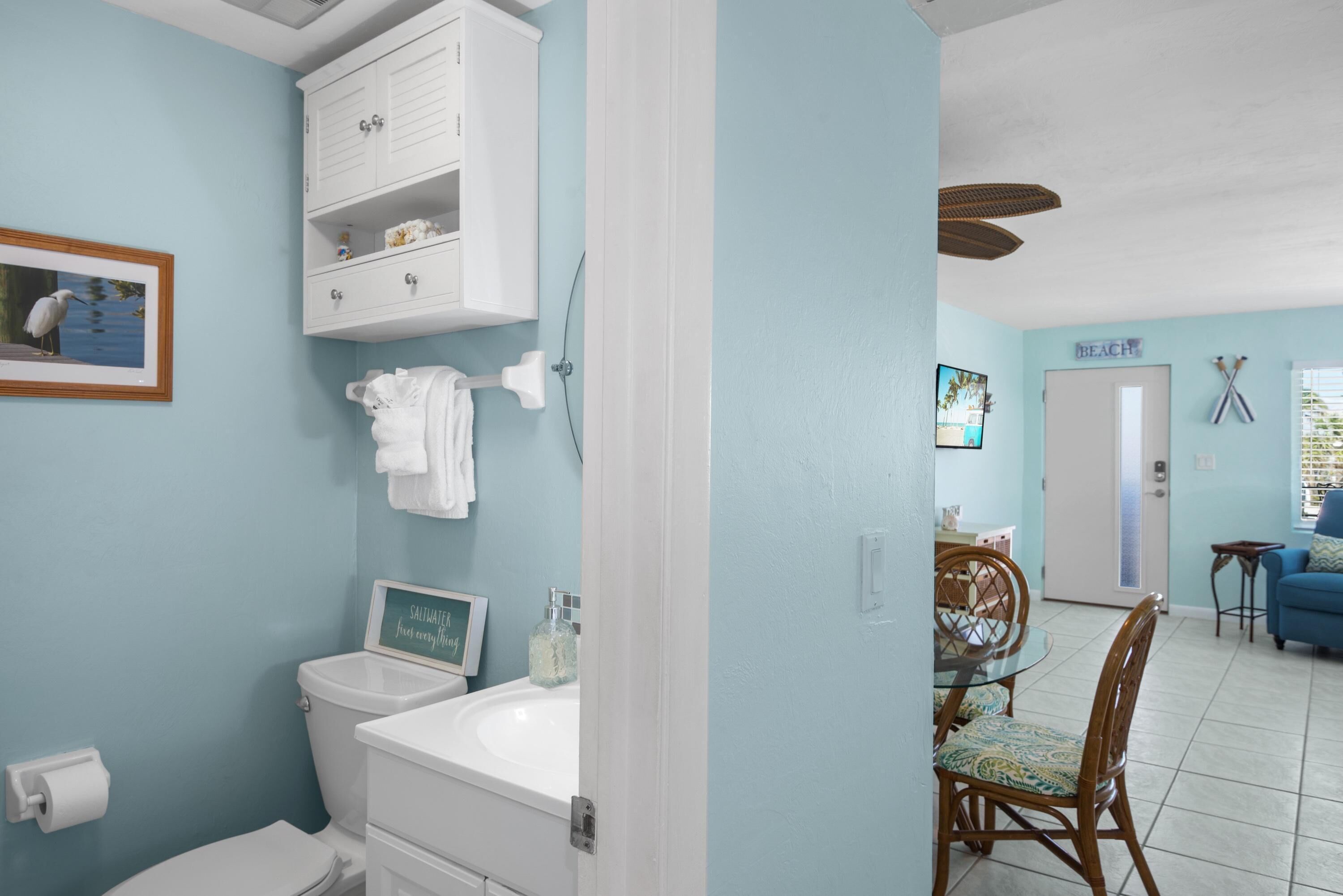 A bathroom with a toilet, sink, and cabinet. There is a towel rack and a framed picture on the wall.