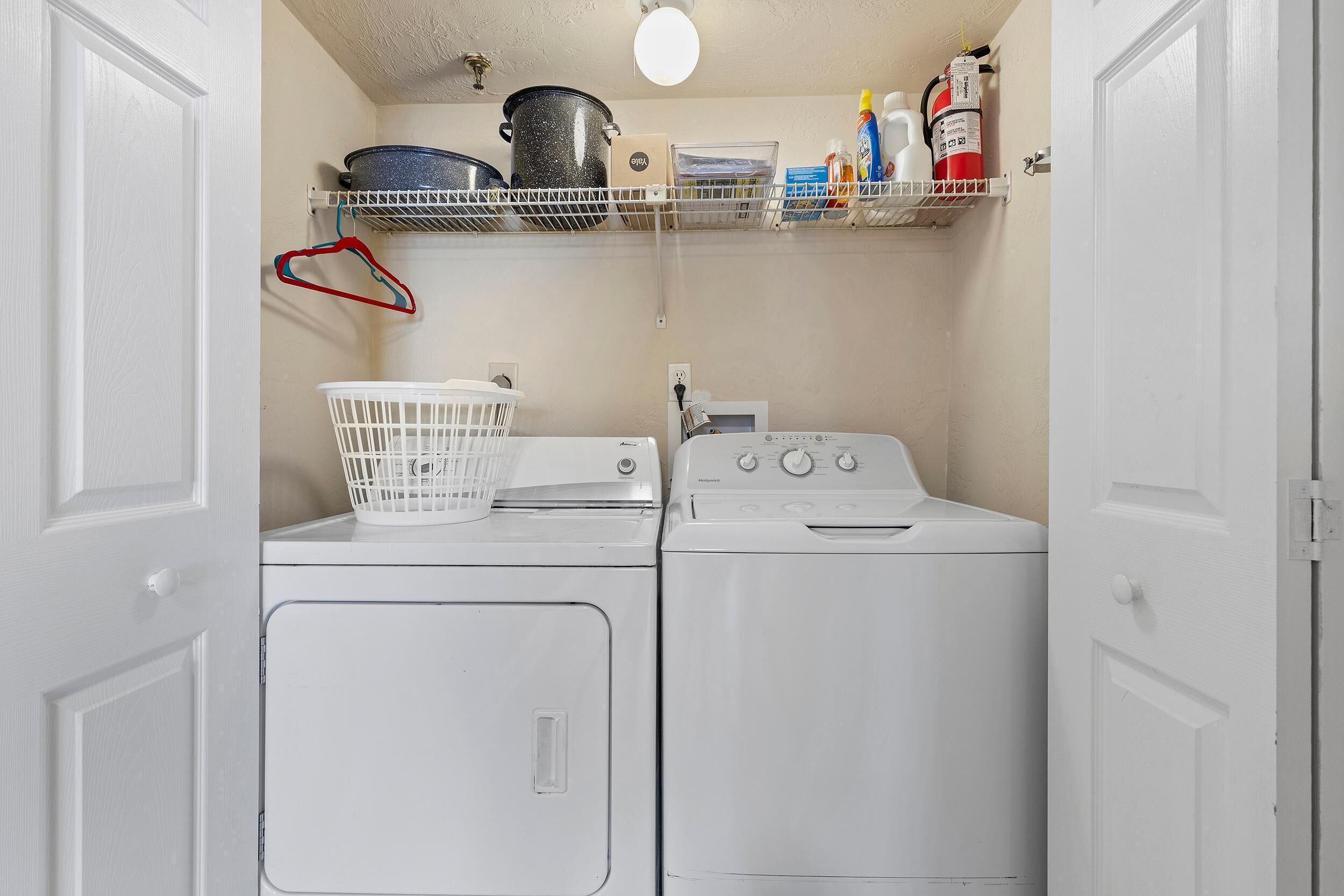 A laundry room with two washing machines, a basket, and shelves with cleaning supplies.
