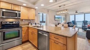 A modern kitchen with stainless steel appliances, wooden cabinets, and a granite countertop. - Sunrise 302 (New Smyrna Beach)