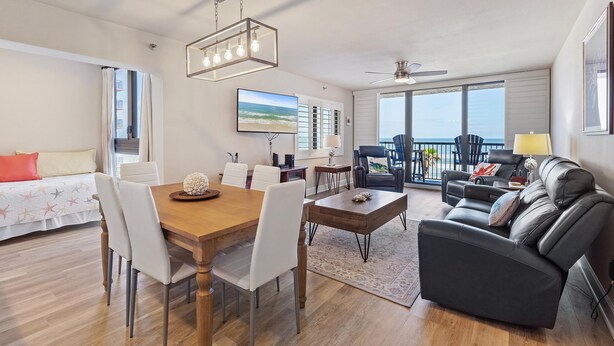 A spacious living area with a dining table, a sofa, and a large window offering a view of the ocean. - Sunrise 302 (New Smyrna Beach)