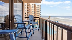 A balcony with blue Adirondack chairs, a pool, and a view of the beach and ocean. - Sunrise 302 (New Smyrna Beach)