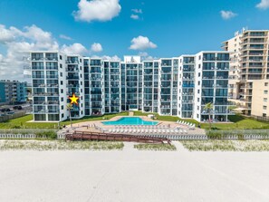 A modern multi-story hotel with a central swimming pool, balconies, and a fenced outdoor area. - Sunrise 302 (New Smyrna Beach)