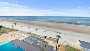 A beach view with a pool area, lounge chairs, and a fenced swimming area. - Sunrise 502 (New Smyrna Beach)