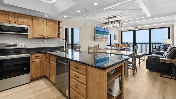 A modern kitchen with wooden cabinets, a stainless steel range, and a large island. - Sunrise 502 (New Smyrna Beach)