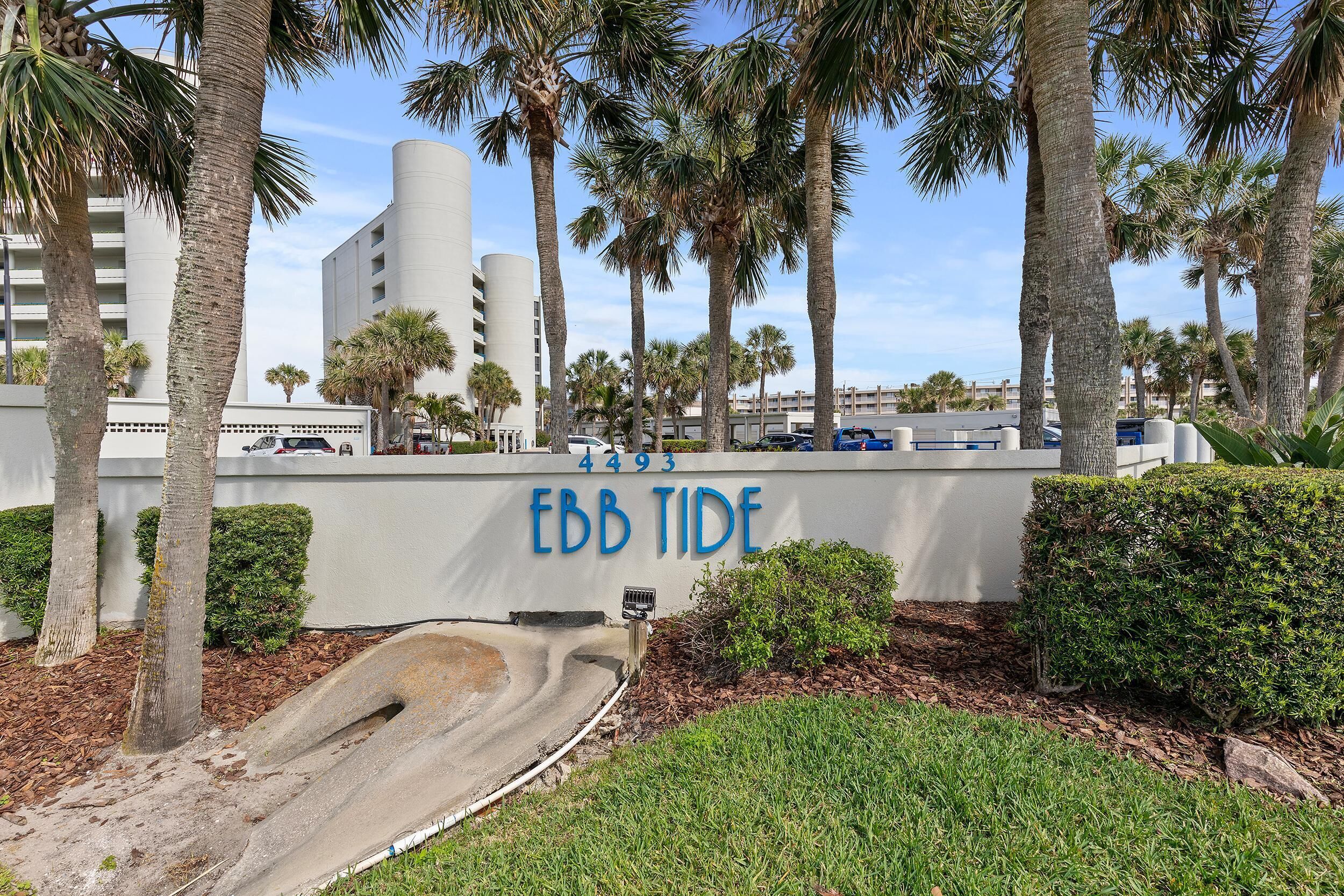 Un letrero con la leyenda 'EBB TIDE' y el número '4493' en una pared, rodeado de palmeras y una zona verde.