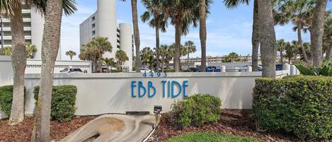 Un letrero con la leyenda 'EBB TIDE' y el número '4493' en una pared, rodeado de palmeras y una zona verde.