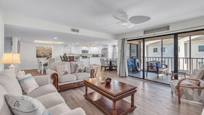 A spacious living room with a wooden coffee table, a sofa, and a dining area with a chandelier. - Sea Club #46 - Coastal Gem (Indian Shores)
