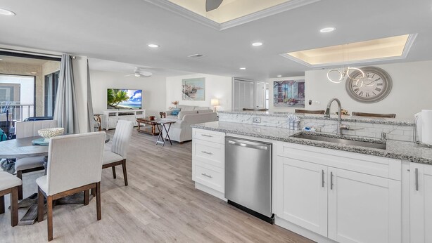 A modern kitchen with white cabinetry, a stainless steel dishwasher, and a large island with a sink. - Sea Club #46 - Coastal Gem (Indian Shores)