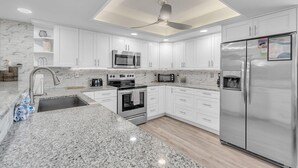 A modern kitchen with white cabinets, granite countertops, stainless steel appliances, and a ceiling fan. - Sea Club #46 - Coastal Gem (Indian Shores)