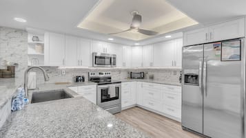 A modern kitchen with white cabinets, granite countertops, stainless steel appliances, and a ceiling fan.