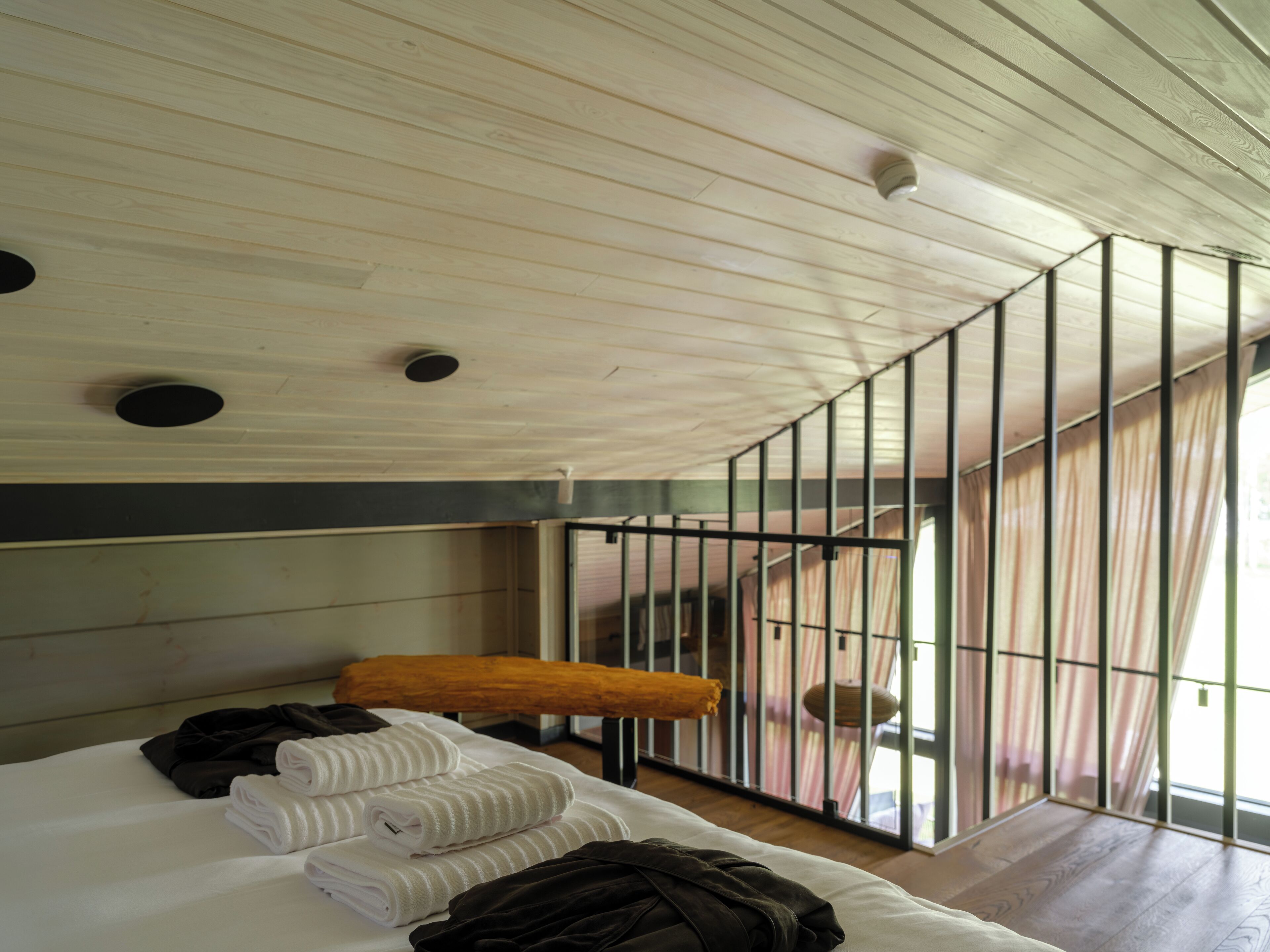 A room with a bed, a bench, and a view of a balcony.